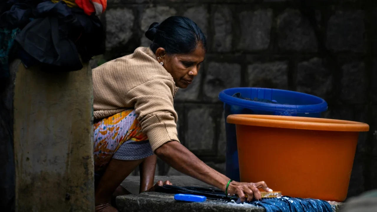 seorang perempuan menyikat pakaian di atas lempengan batu di lantai