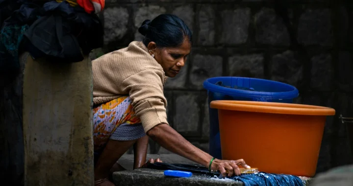 seorang perempuan menyikat pakaian di atas lempengan batu di lantai