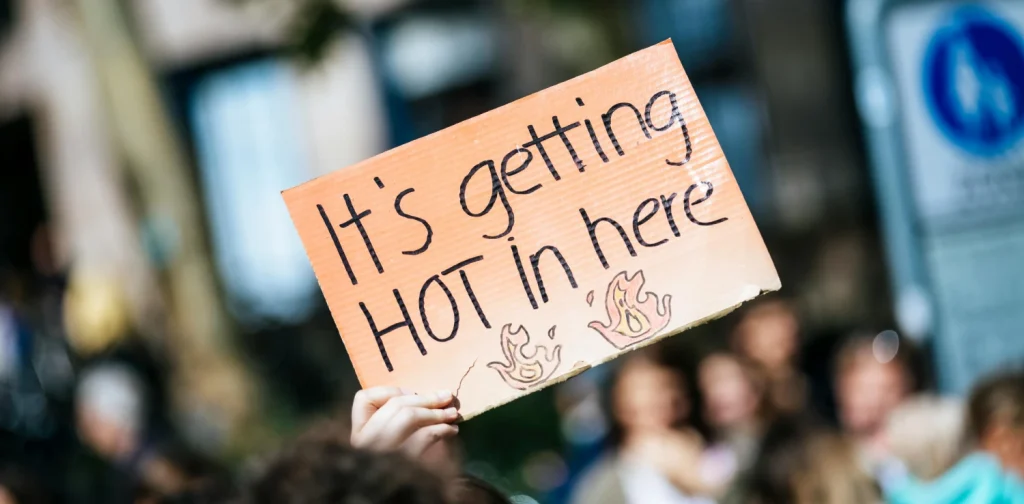 sebuah tangan memegang kertas bertuliskan “it’s getting hot in here”