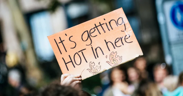 sebuah tangan memegang kertas bertuliskan “it’s getting hot in here”