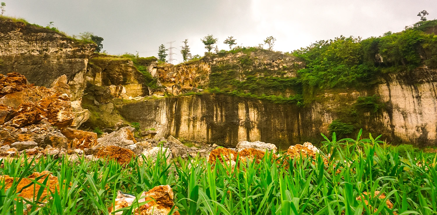 foto bebukitan karst yang rusak dengan bongkahan-bongkahan batu dan beberapa tanaman jagung di sekitarnya.