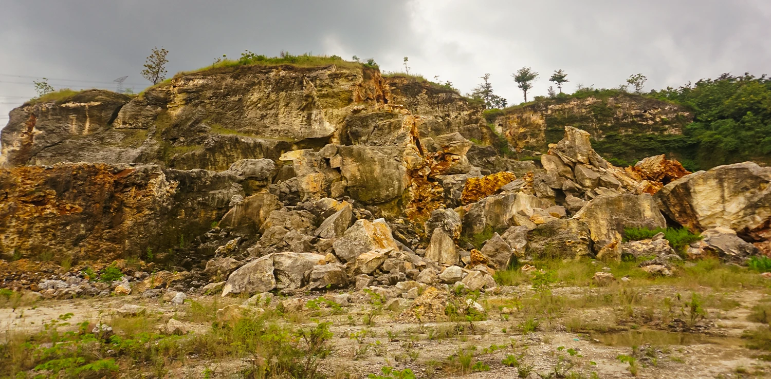 foto bebukitan karst yang rusak dengan bongkahan-bongkahan batu di sekitarnya.