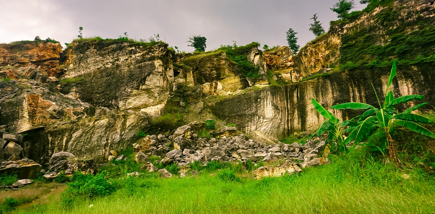 foto bebukitan karst yang rusak dengan bongkahan-bongkahan batu dan beberapa tanaman serta rumput di sekitarnya.