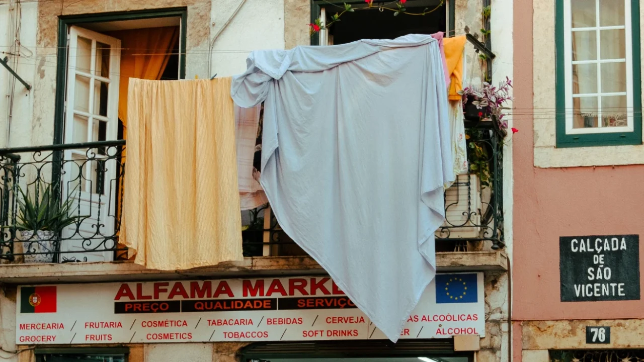 Seprai berwarna oranye dan putih dijemur menggantung dari jendela lantai dua sebuah toko di pasar lokal di Alfama, Lisbon.