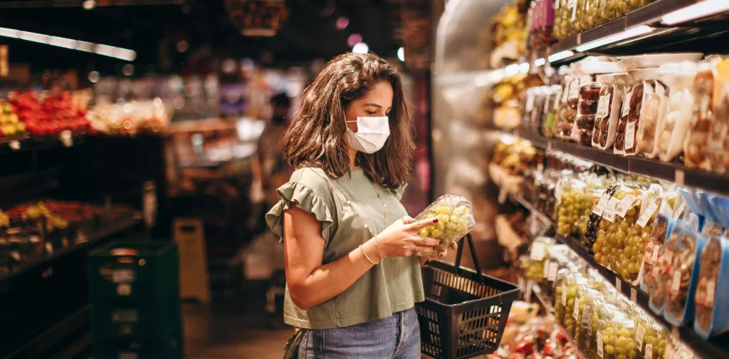 Seorang perempuan muda bermasker sedang memilih buah-buahan di lorong produk segar di supermarket