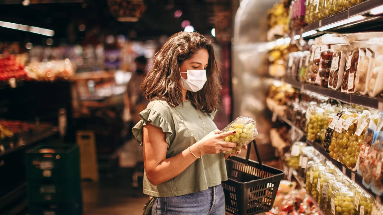 Seorang perempuan muda bermasker sedang memilih buah-buahan di lorong produk segar di supermarket
