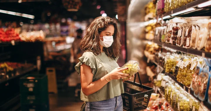 Seorang perempuan muda bermasker sedang memilih buah-buahan di lorong produk segar di supermarket