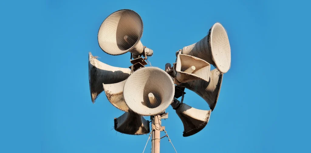 Foto jarak dekat beberapa megaphone tua pada sebuah tiang dengan latar belakang langit biru cerah