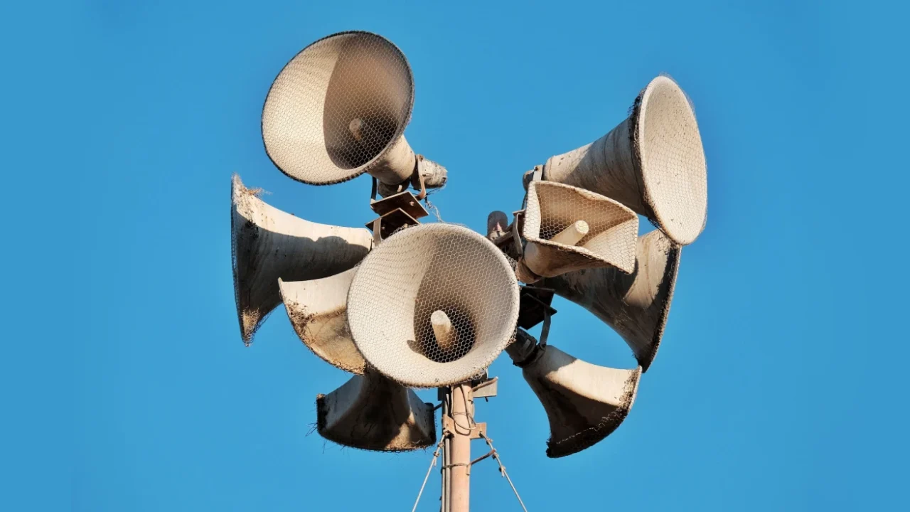 Foto jarak dekat beberapa megaphone tua pada sebuah tiang dengan latar belakang langit biru cerah